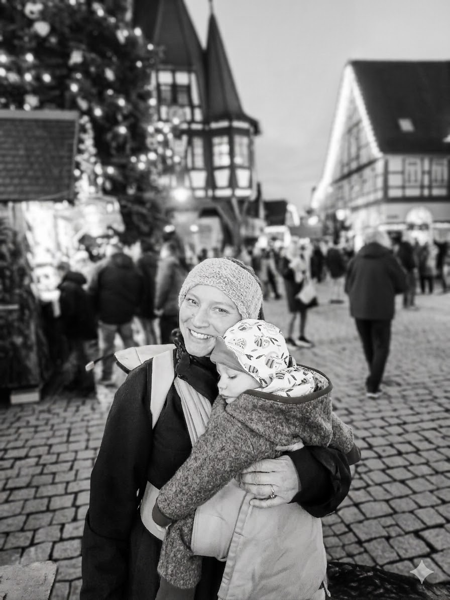 Lächelnde Frau mit kleinem Kind in der Trage, im Hintergrund ein beleuchteter Marktplatz